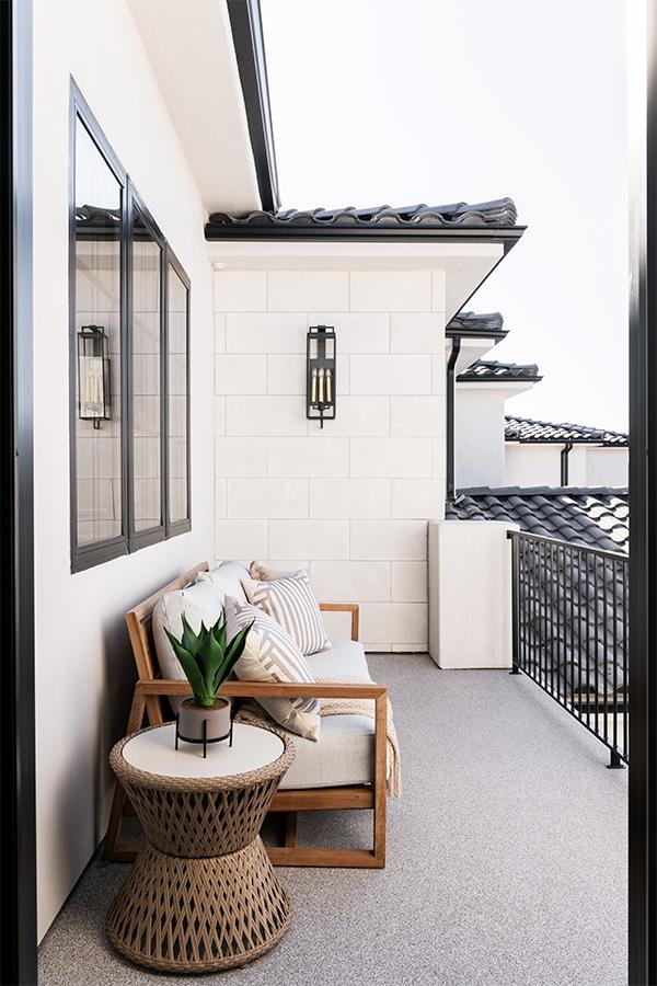 A balcony with a couch and side table on a Spanish mission-style home with a black tile roof, white walls, and black windows.