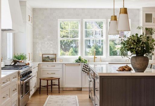 A kitchen with white zellige tile, a large wood island, and a bank of three white windows above the sink.