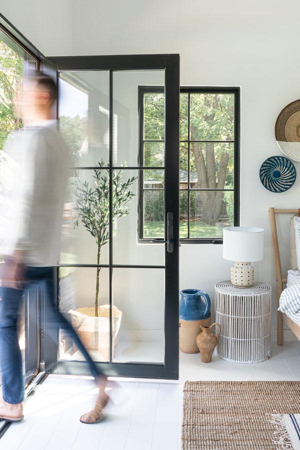 Two interior shots of a bedroom featuring a set of black E-Series Hinged Patio Doors that opens up to a deck and swimming pool outside.