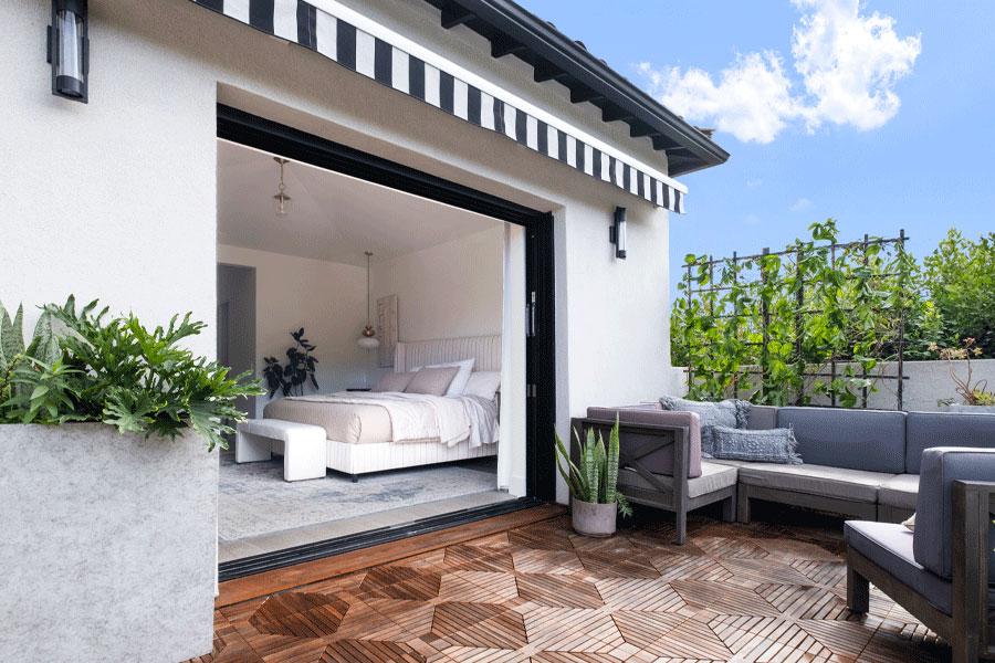 An outdoor view of a bedroom that’s connected to the adjacent balcony all decked out with outdoor couches for lounging.