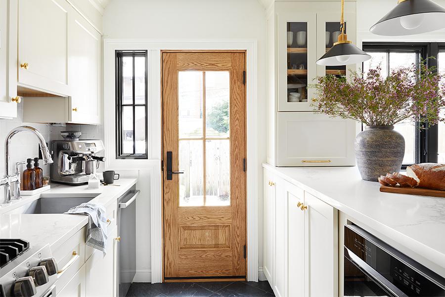  A kitchen with white painted cabinetry, white quartz counters, and a natural wood front door featuring a large glass panel with grilles.