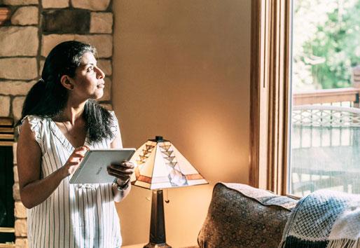 woman looking out window holding an ipad