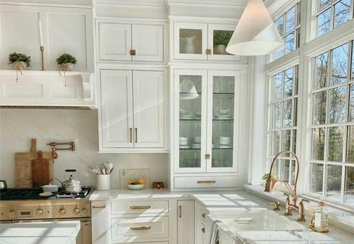 Light streams into an all-white kitchen through sparkling clean windows.