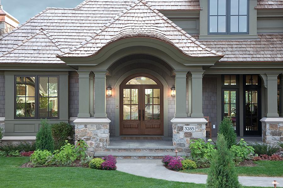 A traditional shingle-style colonial home with a deep front porch and a double front door with transom above it.