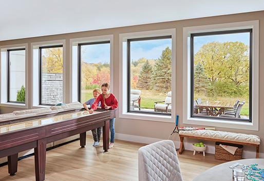 Two children play shuffleboard in a walkout basement with wood floors and a row of five picture windows behind them.