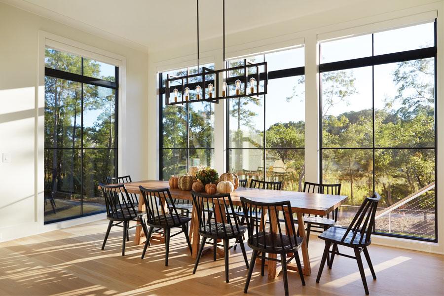 Fall light streams through large black framed windows into a dining room.