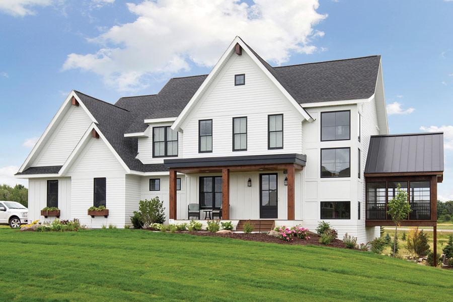 A modern farmhouse with white exterior and black windows stands out against a vibrant green lawn