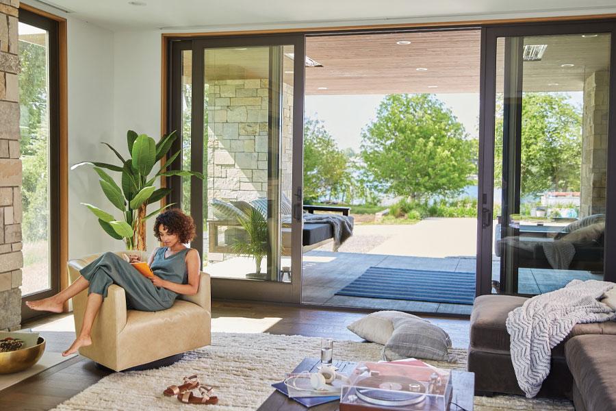 A woman lounges next to an open sliding glass door with a lake view.