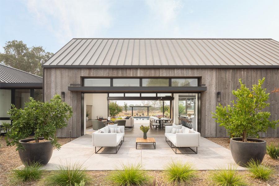 An exterior shot showing a home with moving glass wall systems on two walls so the front yard patio, living room, and backyard swimming pool are all one combined space.