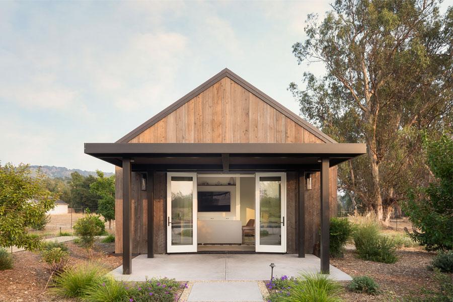 An ADU with cedar siding and a four-panel hinged patio door that opens to a patio covered by a metal pergola.