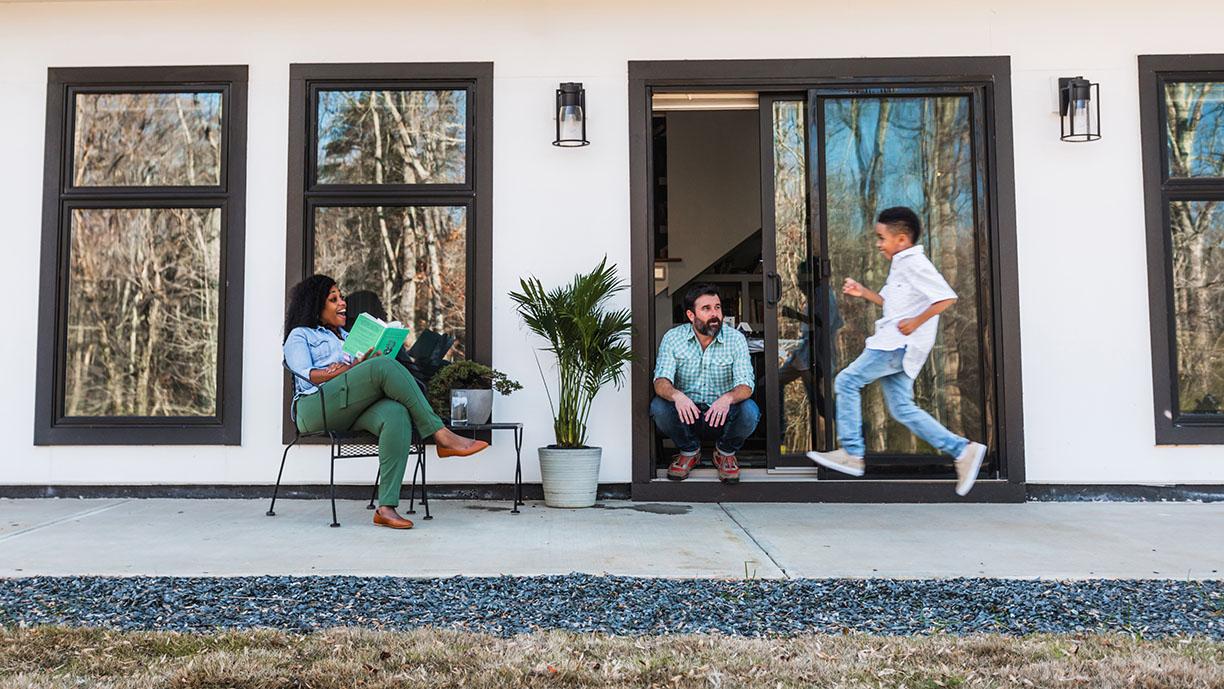 man and woman sitting in front of andersen gliding patio door watching child run