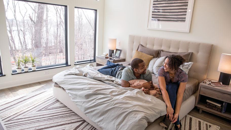 Interior of modern bedroom with a couple in front of Andersen picture windows with a nature view